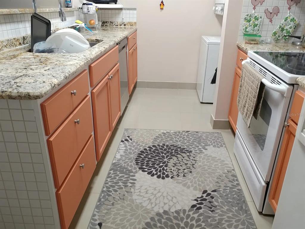 A kitchen features orange cabinets, granite countertops, a white stove, and a floral-patterned area rug — 2225 HOLDEN AVENUE UNIT 109, ORLANDO, FL