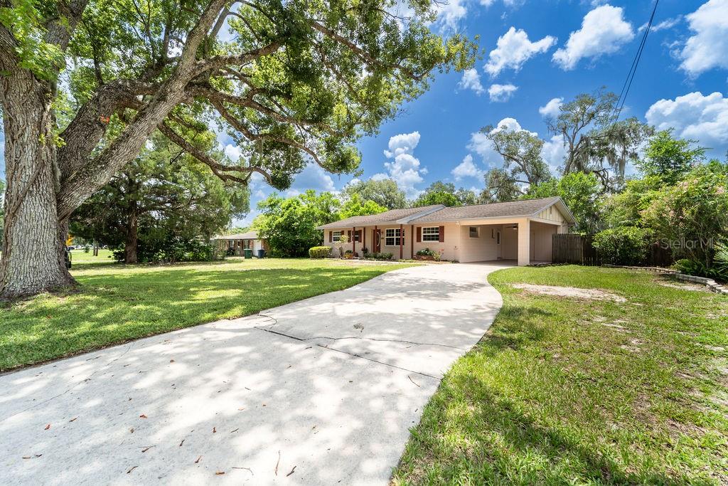 A single-story house with a concrete driveway, a carport, and large trees in the yard — 686 E KENTUCKY AVENUE, DELAND, FL
