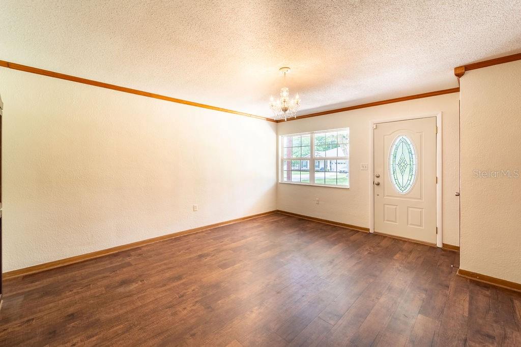 An empty room with wood-look flooring, white walls, a chandelier, and a front door — 686 E KENTUCKY AVENUE, DELAND, FL