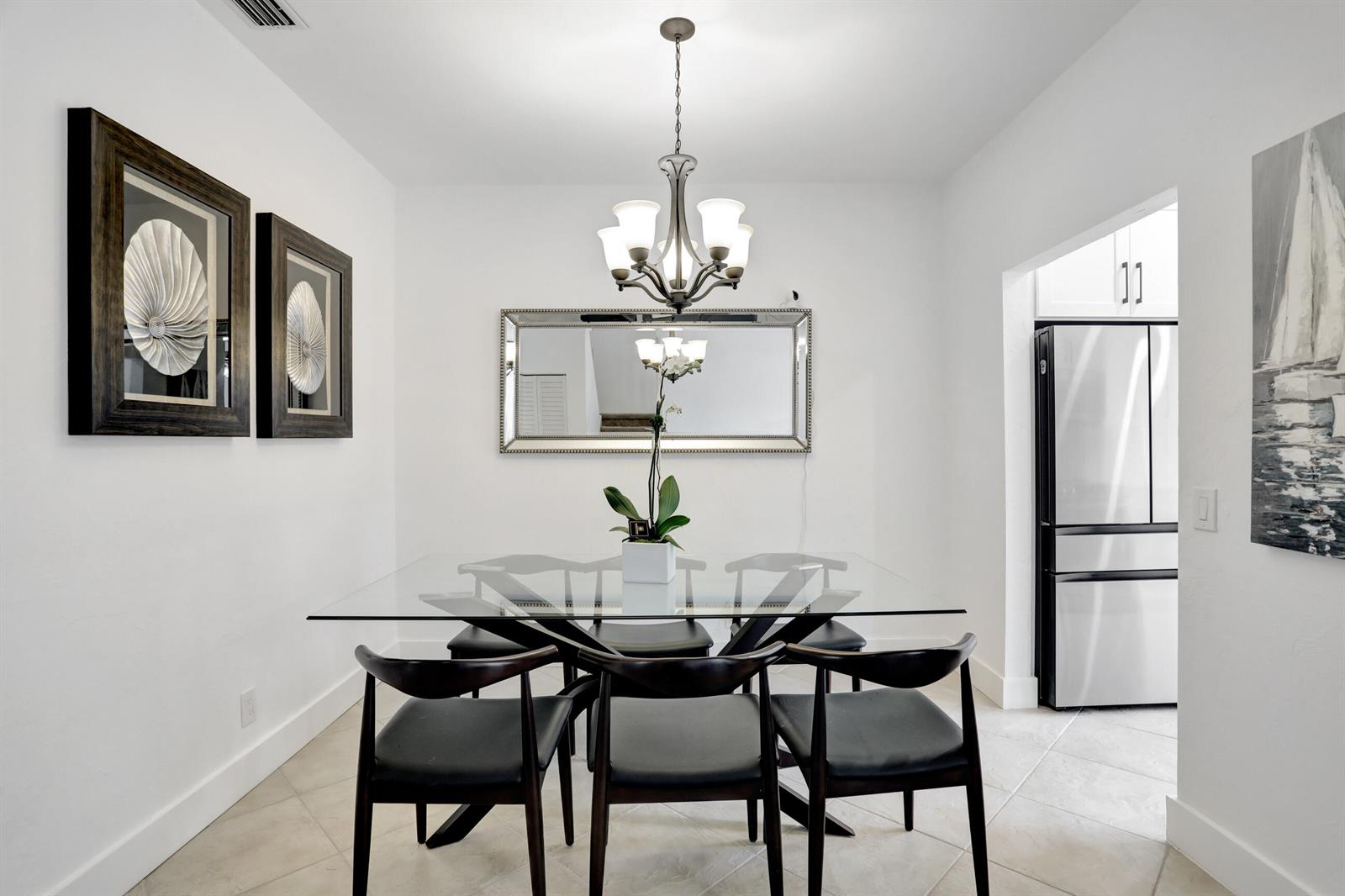 A dining room features a glass-top table, six black chairs, a chandelier, and wall art — 6770 Via Regina, Boca Raton FL 33433, BOCA RATON, FL