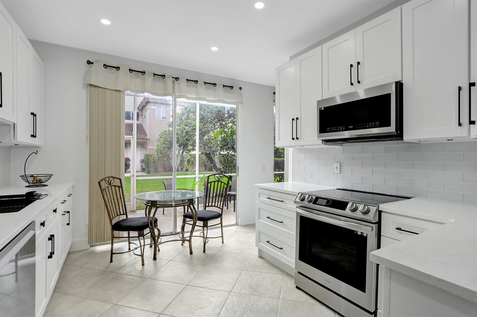 A bright kitchen features white cabinets, stainless steel appliances, and a small dining area — 6770 Via Regina, Boca Raton FL 33433, BOCA RATON, FL