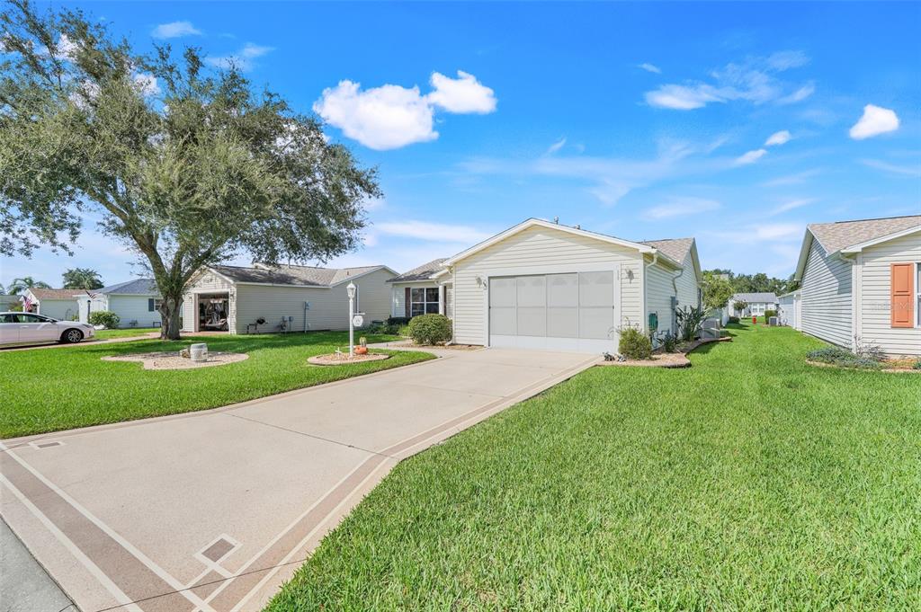 A single-story house with a concrete driveway and a large tree in the front yard — 870 HENDERSON LANE, THE VILLAGES, FL