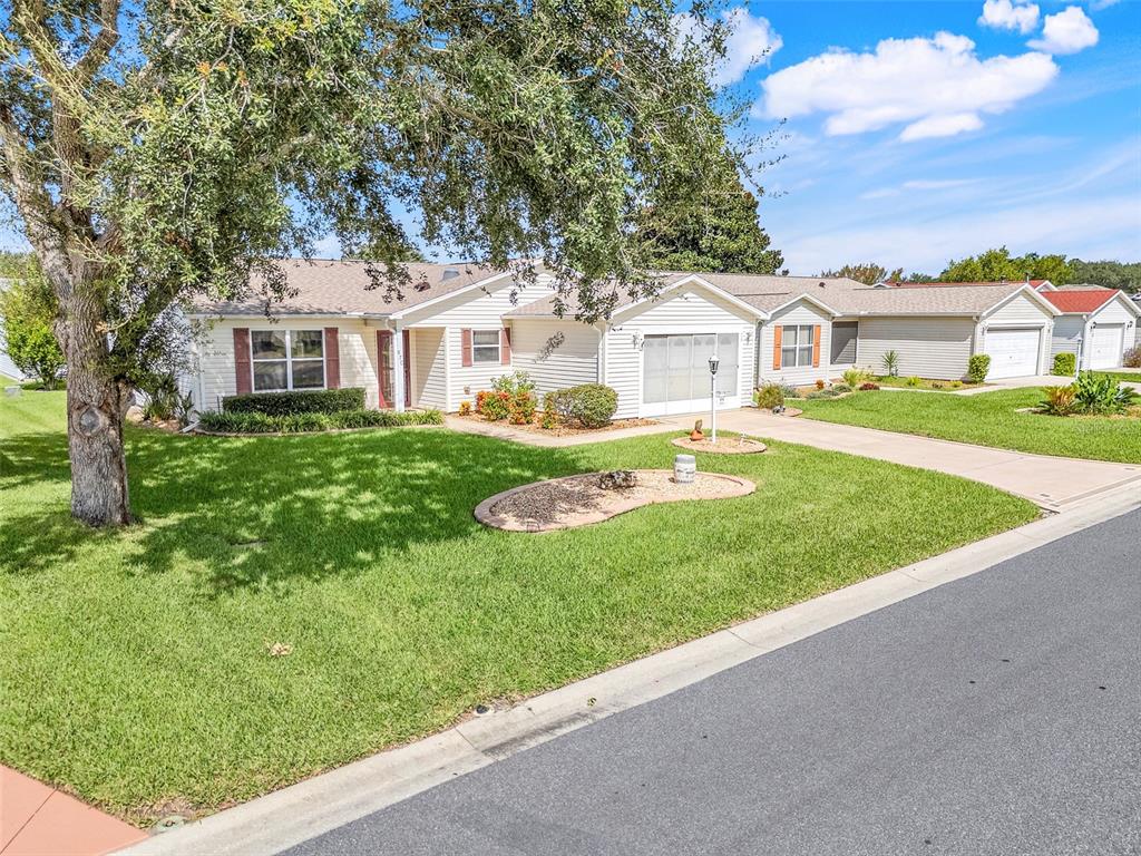 A single-story house with light siding, a garage, and a large tree in the yard — 870 HENDERSON LANE, THE VILLAGES, FL