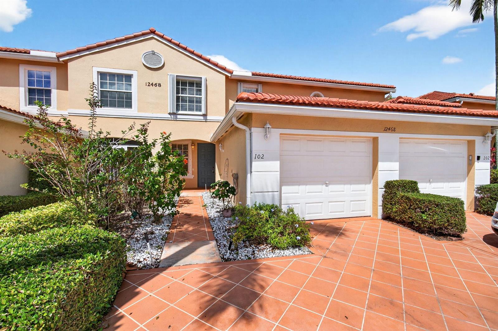 A two-story townhouse with a tan stucco exterior, red tile roof, and a paved driveway — 12468 Crystal Pointe Drive # 102, Boynton Beach FL 33437, BOYNTON BEACH, FL