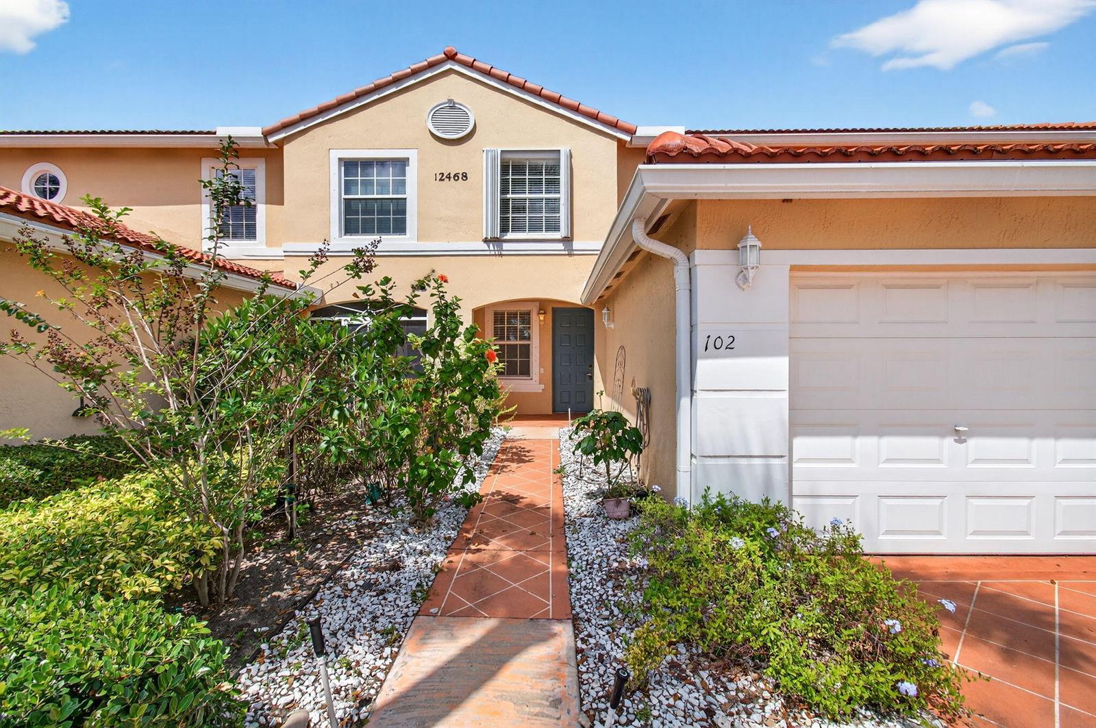 A two-story stucco townhouse features a tile roof, a garage, and a front walkway — 12468 Crystal Pointe Drive # 102, Boynton Beach FL 33437, BOYNTON BEACH, FL
