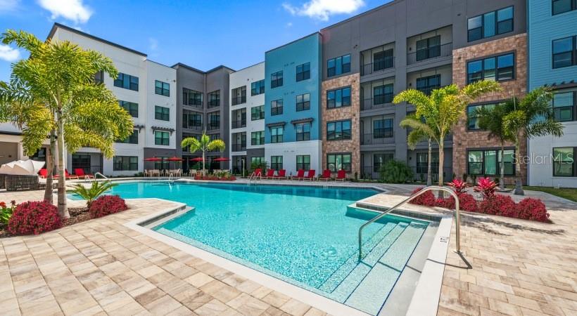 A swimming pool sits in the courtyard of a multi-story apartment building with palm trees — 8925 77TH TERRACE E UNIT A4, LAKEWOOD RANCH, FL