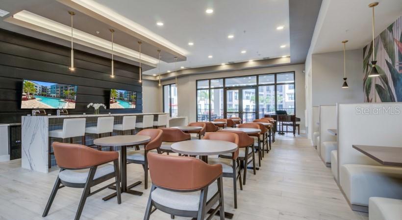 A modern apartment clubhouse lounge features a marble bar, café tables, and booth seating — 8925 77TH TERRACE E UNIT A4, LAKEWOOD RANCH, FL