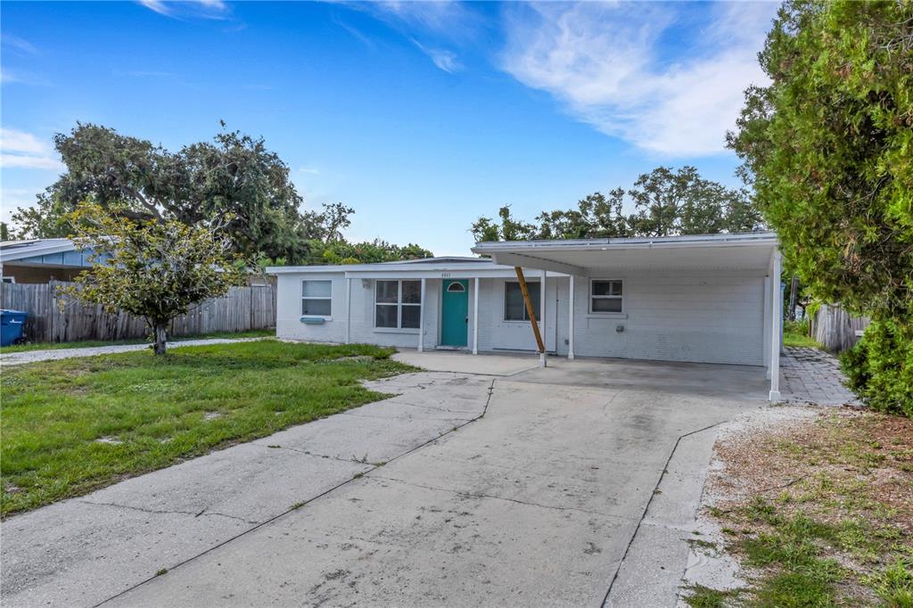 A white single-story house features a teal front door, a concrete driveway, and a carport — 4861 BELL MEADE DRIVE, SARASOTA, FL