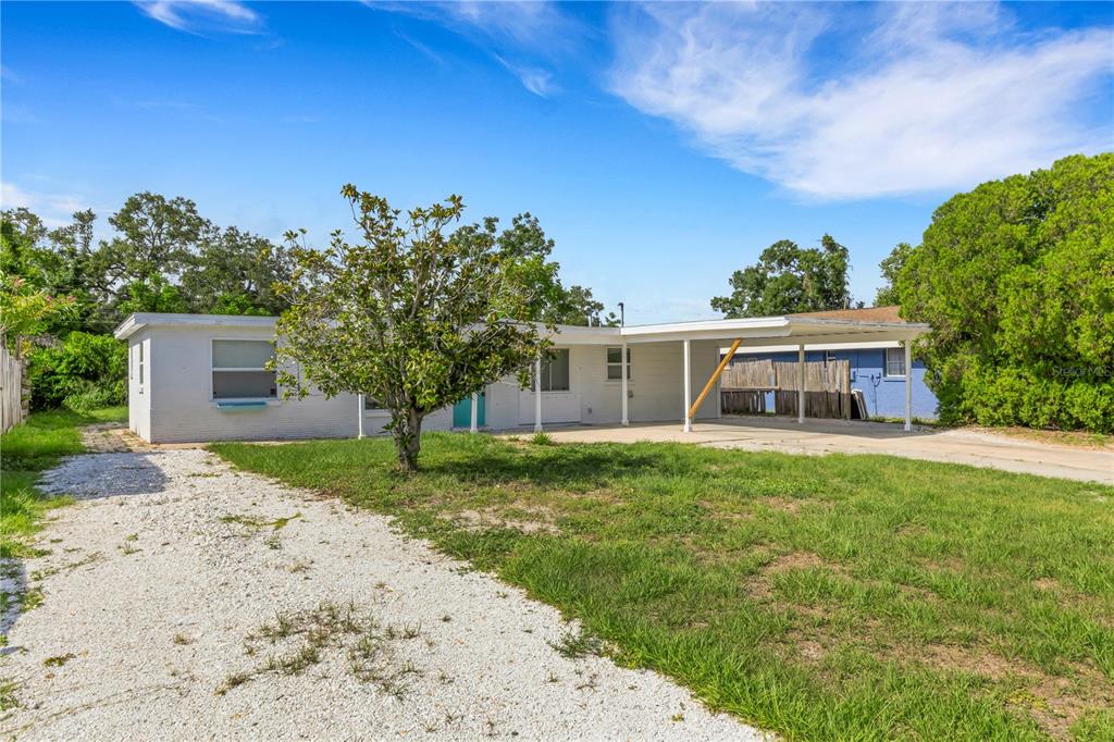 A white, single-story house features a gravel driveway, a front yard tree, and a carport — 4861 BELL MEADE DRIVE, SARASOTA, FL