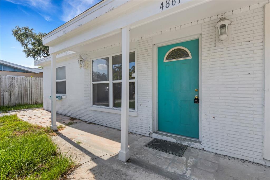 A white brick house exterior features a bright teal front door and a covered porch — 4861 BELL MEADE DRIVE, SARASOTA, FL