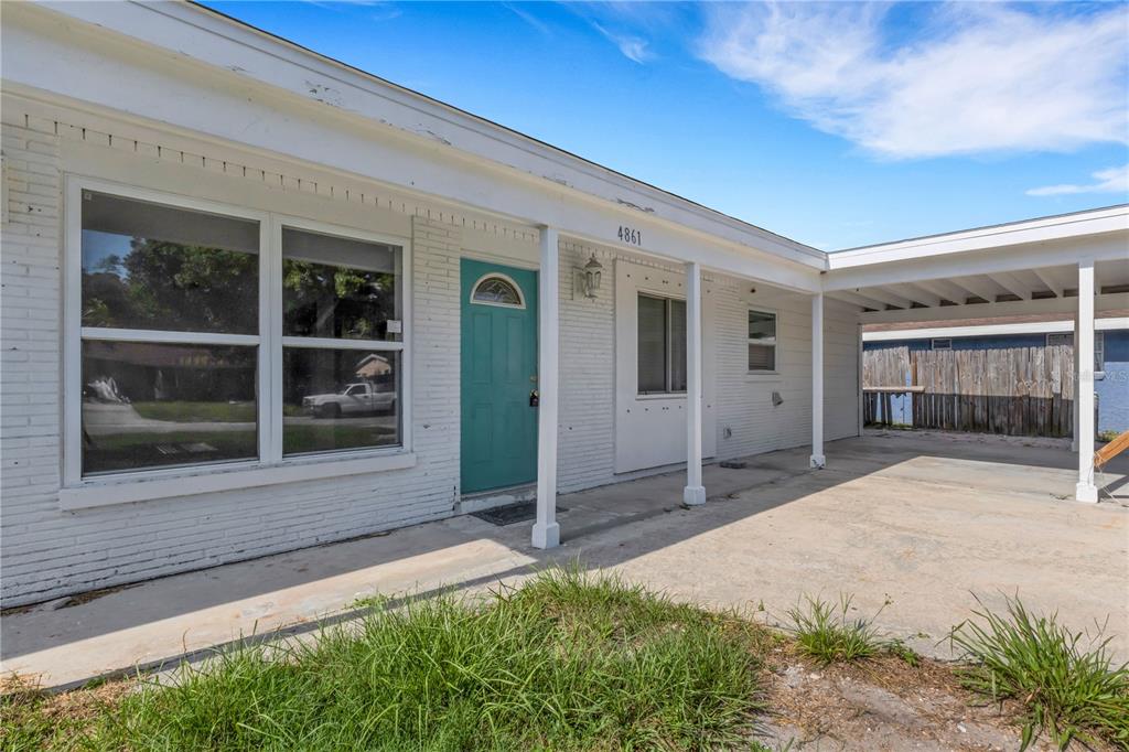 A white brick house exterior features a teal front door and an attached carport — 4861 BELL MEADE DRIVE, SARASOTA, FL