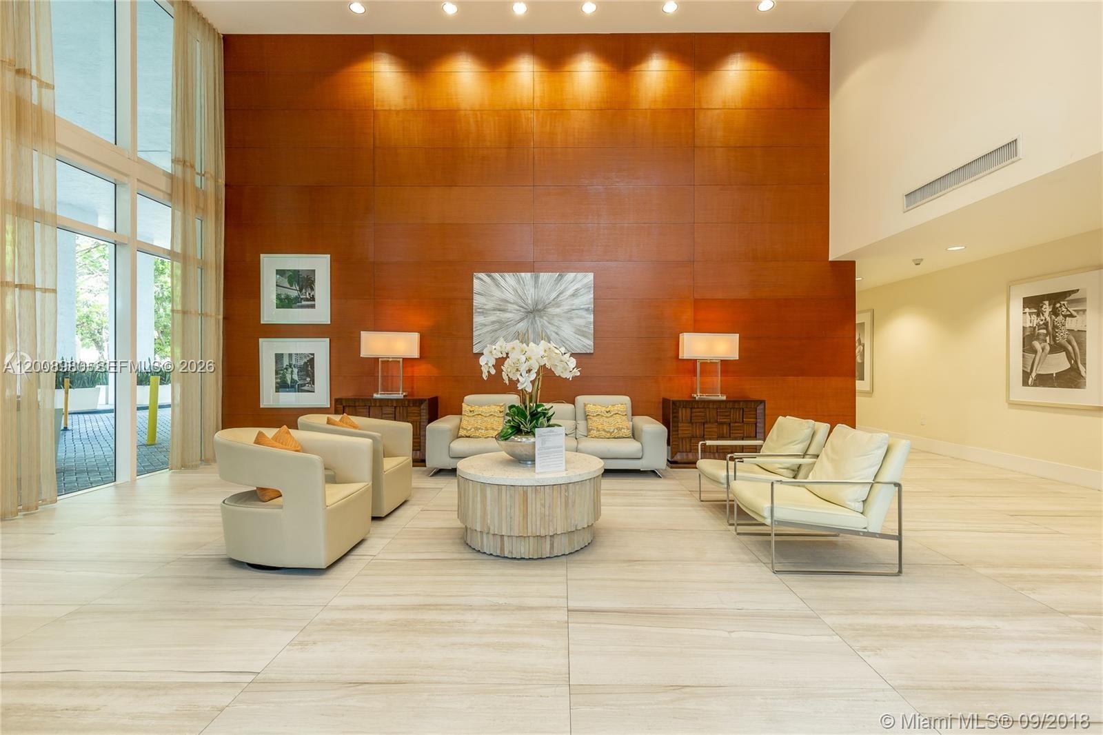 A modern lobby features a large wood-paneled wall, neutral seating, and floor-to-ceiling windows — 1871 NW S River Dr # 902, Miami FL 33125, MIAMI, FL