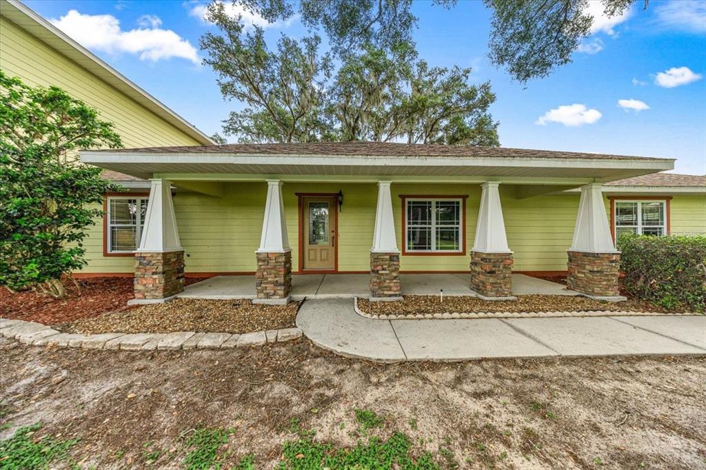 A light green house with a covered front porch featuring stone-based columns and a walkway — 5065 NW 150TH AVENUE, MORRISTON, FL