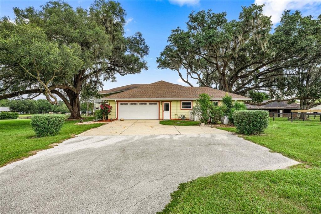A single-story house with a two-car garage and light green siding sits under large trees — 5065 NW 150TH AVENUE, MORRISTON, FL
