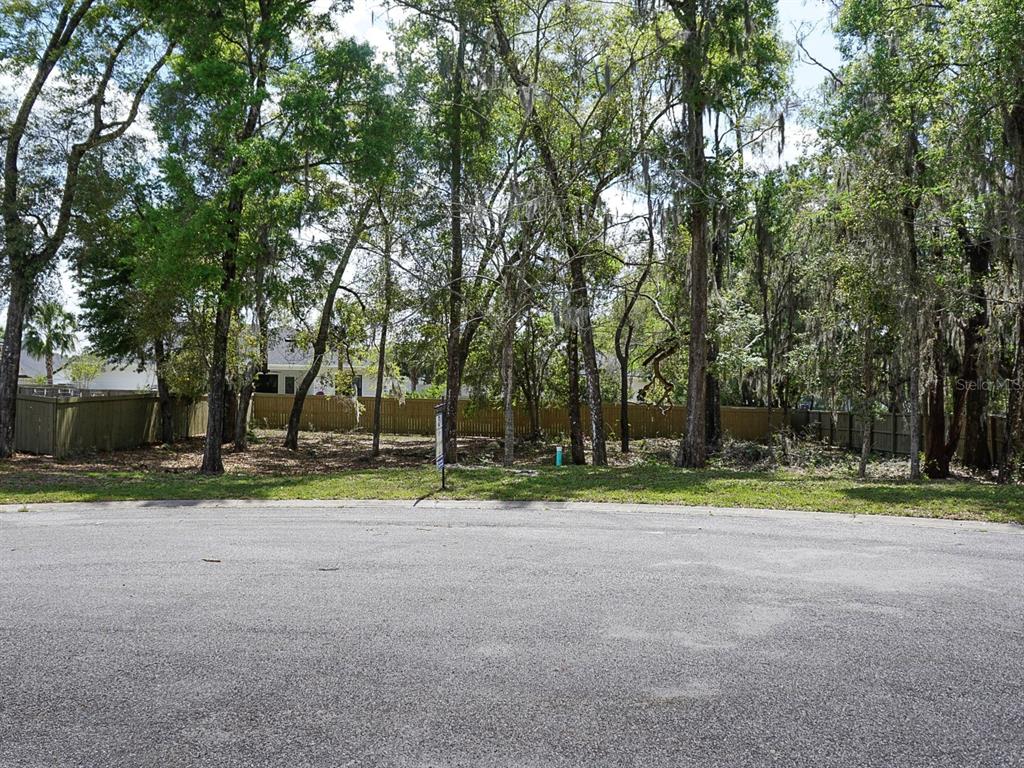 A vacant, wooded residential lot sits behind a paved cul-de-sac and a wooden fence — 12149 SW 9TH LANE, GAINESVILLE, FL