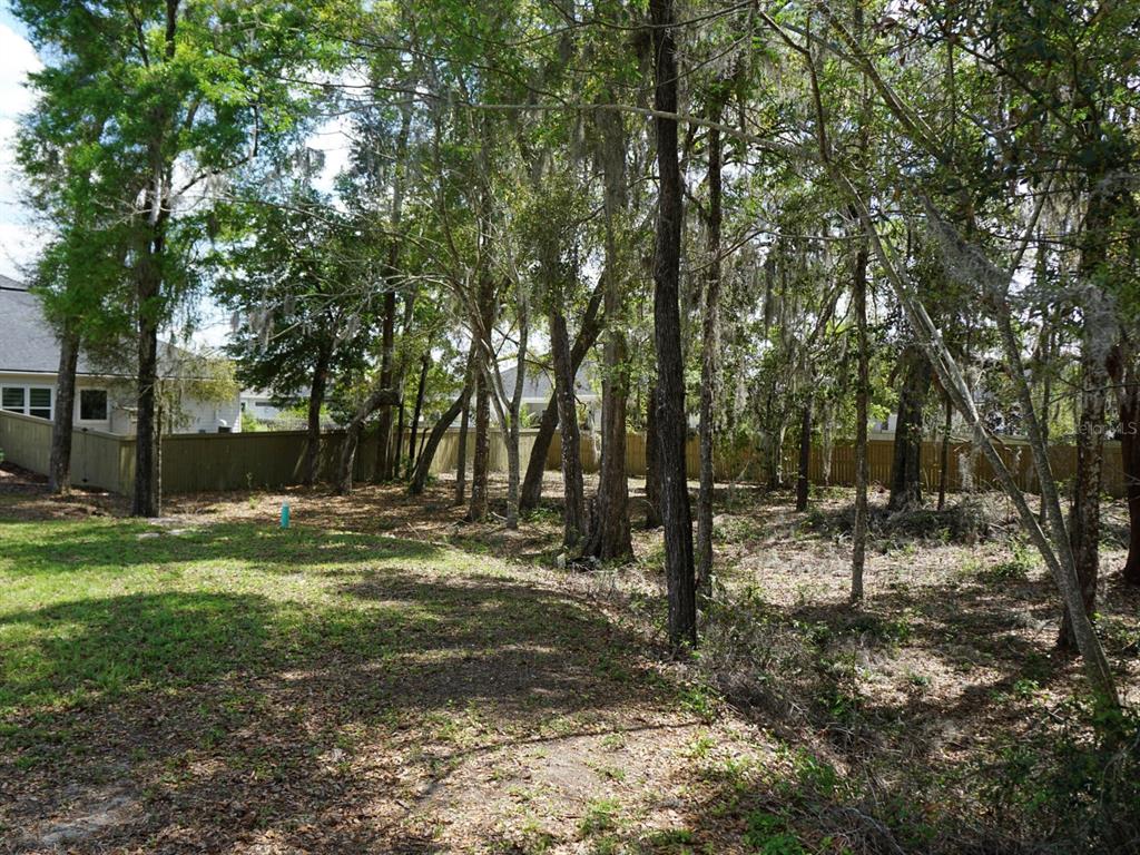 A grassy backyard features a wooded area with mature trees and a wooden privacy fence — 12149 SW 9TH LANE, GAINESVILLE, FL