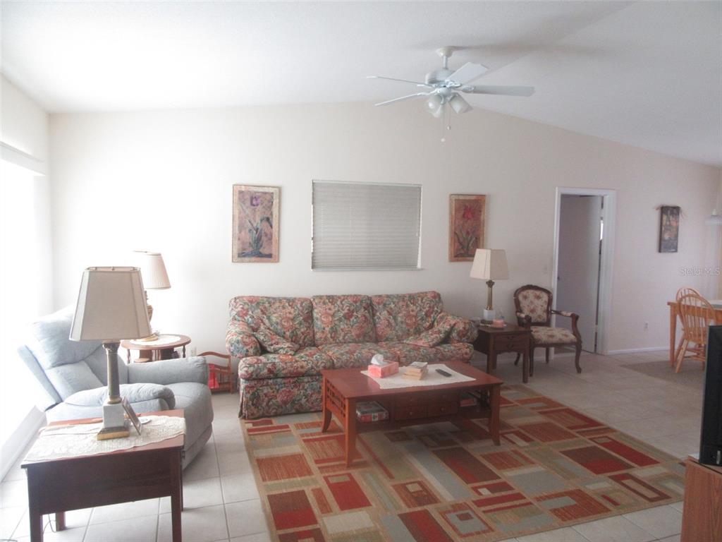 A living room features a floral sofa, a patterned area rug, and a ceiling fan — 8158 FAY AVENUE, NORTH PORT, FL