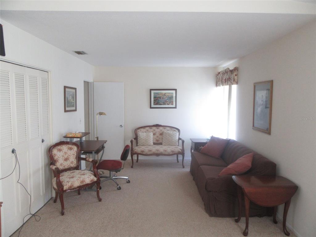 A living room features a brown sofa, a floral settee, a desk, and carpeted flooring — 8158 FAY AVENUE, NORTH PORT, FL