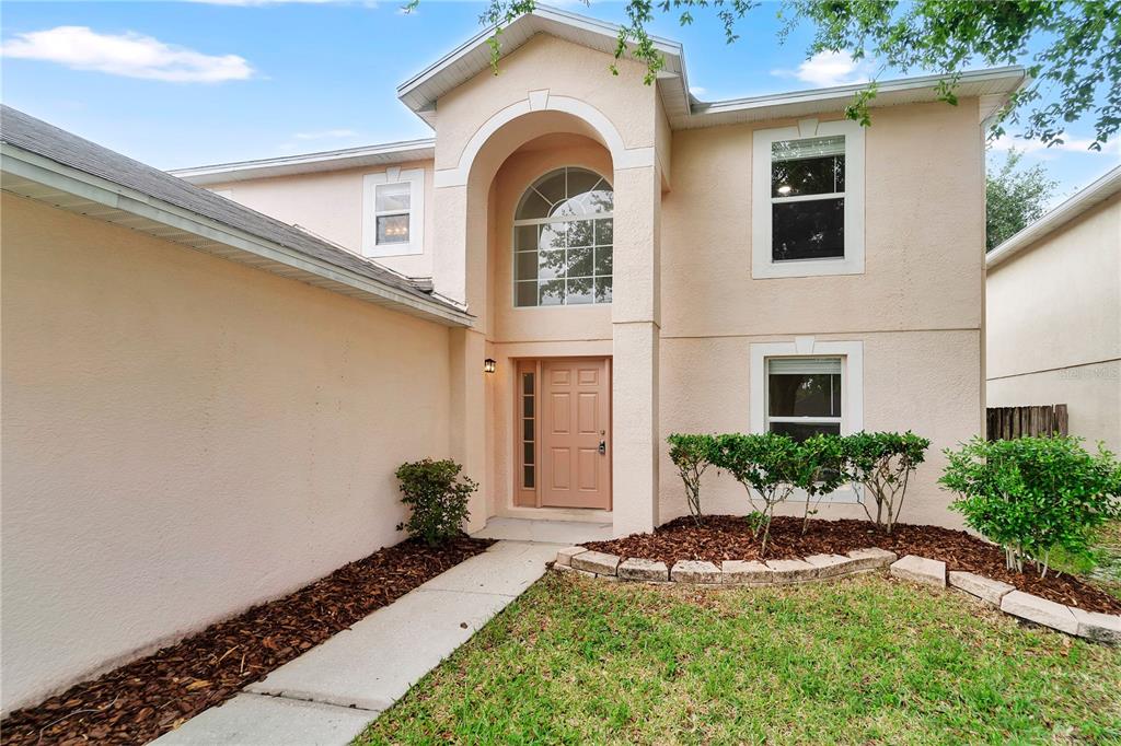 A two-story house with a tan stucco exterior, arched entryway, and a front lawn — 30131 RATTANA COURT, WESLEY CHAPEL, FL