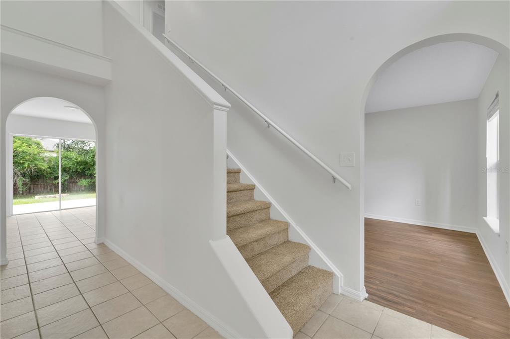 A staircase with beige carpet leads upward between a tiled entryway and a wood-floored room — 30131 RATTANA COURT, WESLEY CHAPEL, FL