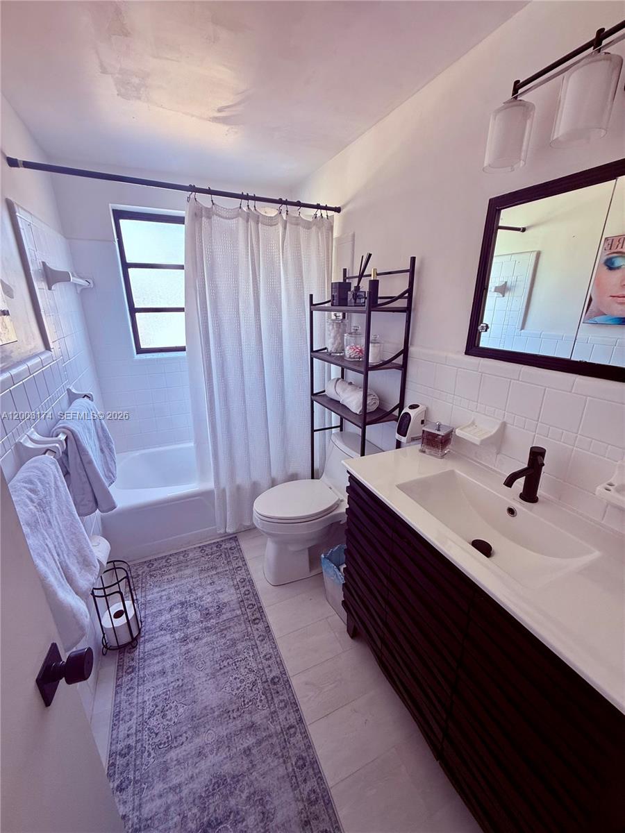 A bathroom features a dark wood vanity, a white tub-shower combo, and a patterned rug — 115 S C St # 101, Lake Worth FL 33460, LAKE WORTH, FL