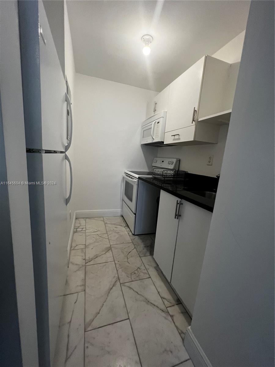 A narrow galley kitchen features white cabinets, black countertops, and light-colored marble-patterned floor tiles — 920 Jefferson Ave # 3, Miami Beach FL 33139, MIAMI BEACH, FL