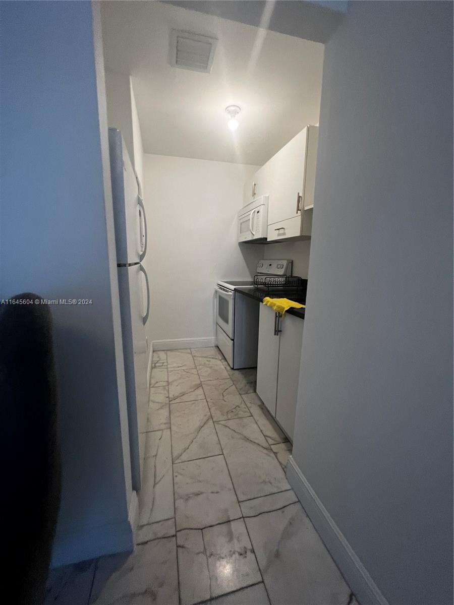 A narrow galley kitchen features white cabinets, white appliances, and light-colored marble-patterned tile flooring — 920 Jefferson Ave # 3, Miami Beach FL 33139, MIAMI BEACH, FL
