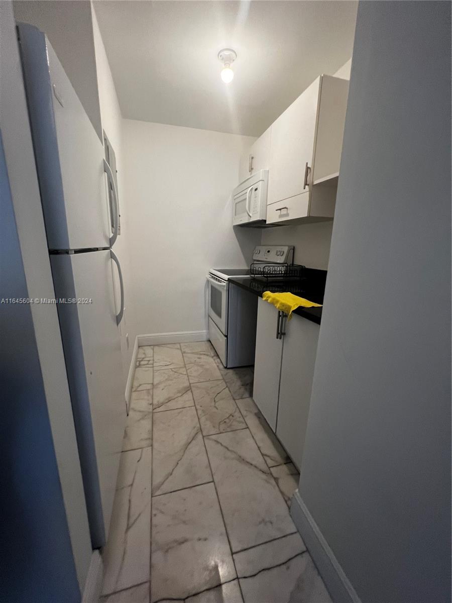 A narrow galley kitchen features white cabinets, a white refrigerator, and black countertops — 920 Jefferson Ave # 3, Miami Beach FL 33139, MIAMI BEACH, FL