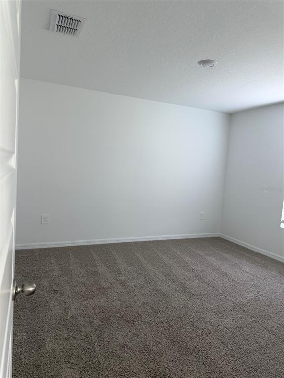 An empty bedroom features gray carpet, white walls, a ceiling light, and an air vent — 1723 GRANDIOSE DRIVE, HAINES CITY, FL