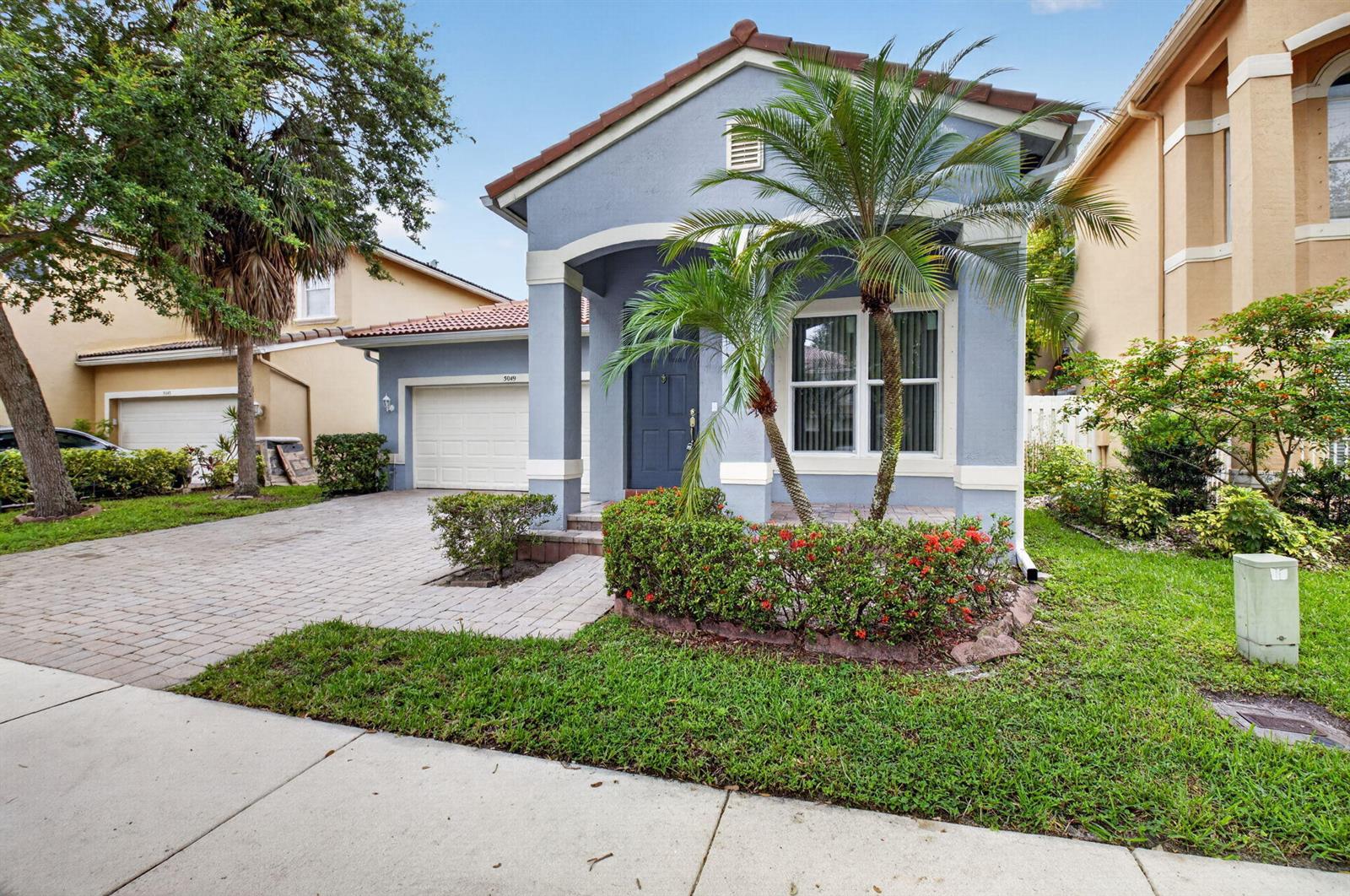 A blue single-story house with a paved driveway, palm trees, and a small front garden — 5049 Sancerre Circle, Lake Worth FL 33463, LAKE WORTH, FL