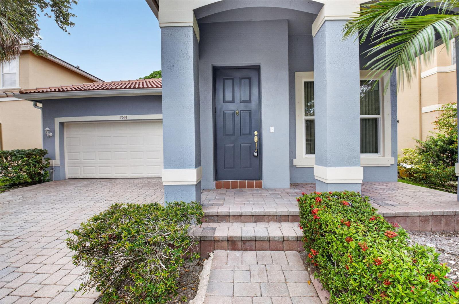 A blue house exterior features a front door, a garage, and a paved walkway — 5049 Sancerre Circle, Lake Worth FL 33463, LAKE WORTH, FL