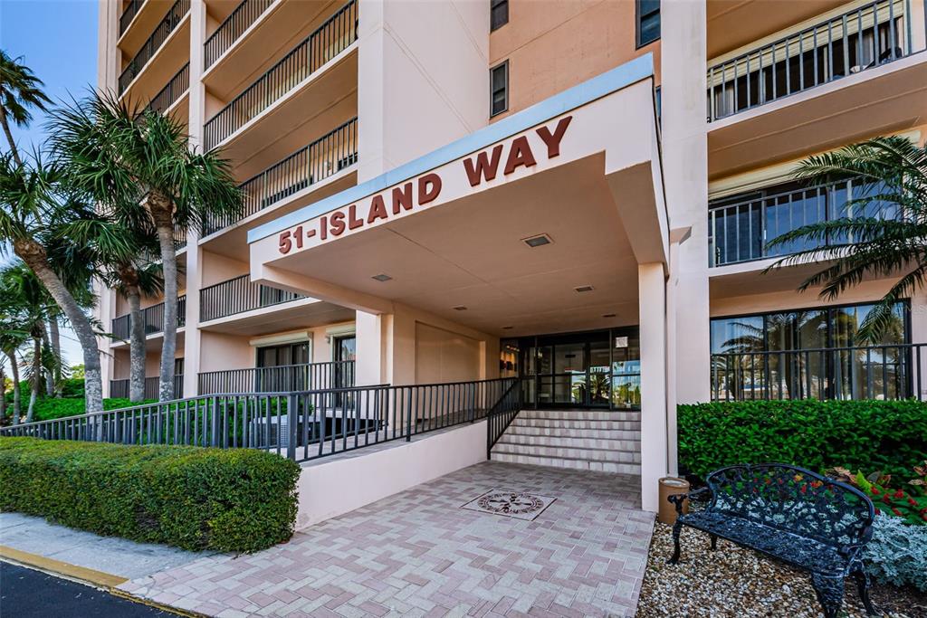The exterior entrance of a multi-story apartment building features a covered walkway and stairs — 51 ISLAND WAY UNIT 306, CLEARWATER BEACH, FL