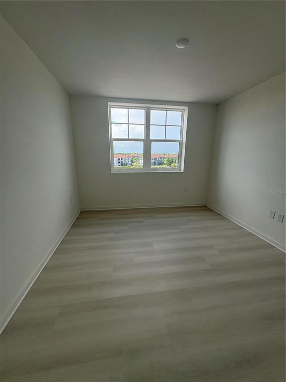 An empty bedroom features light-colored wood-look flooring, white walls, and a window overlooking buildings — 5579 MILLENIA PARK BOULEVARD UNIT 516, ORLANDO, FL