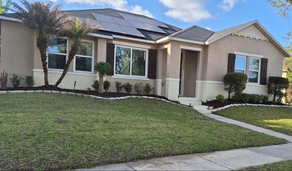 A single-story house with a tan stucco exterior, solar panels, and a landscaped front yard — 14467 GOLDEN RAIN TREE BOULEVARD, ORLANDO, FL