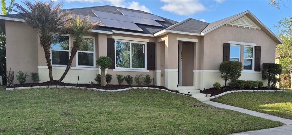 A single-story house with a tan stucco exterior, dark shutters, and roof-mounted solar panels — 14467 GOLDEN RAIN TREE BOULEVARD, ORLANDO, FL