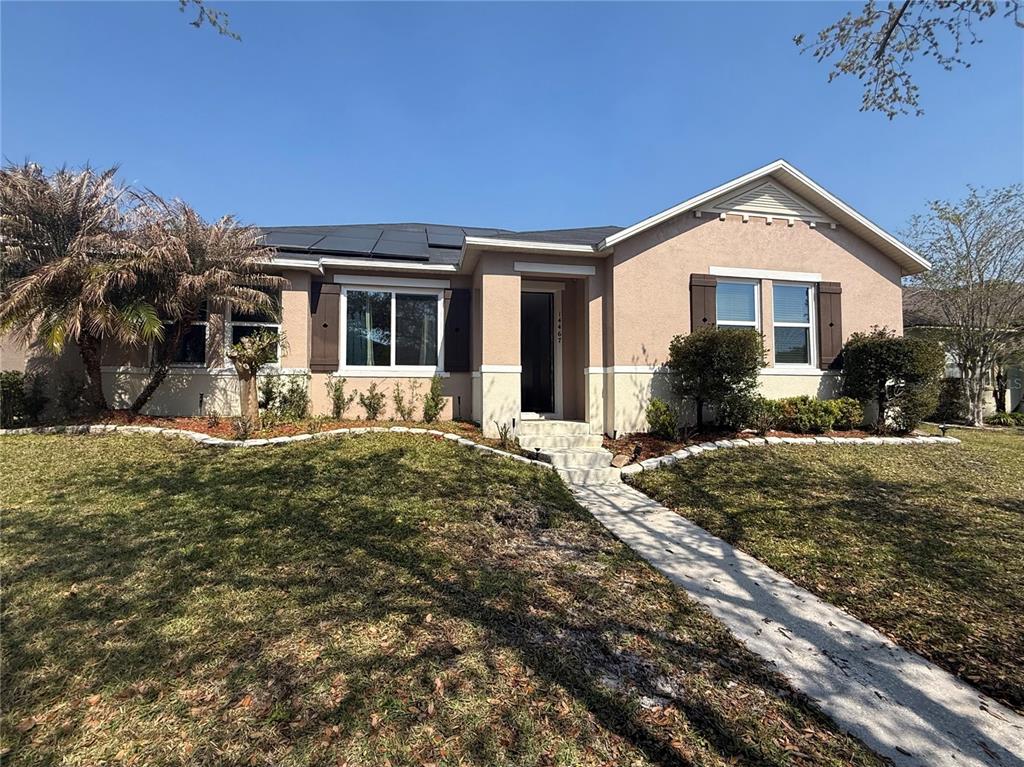 A single-story house with a tan stucco exterior, brown shutters, and solar panels on the roof — 14467 GOLDEN RAIN TREE BOULEVARD, ORLANDO, FL
