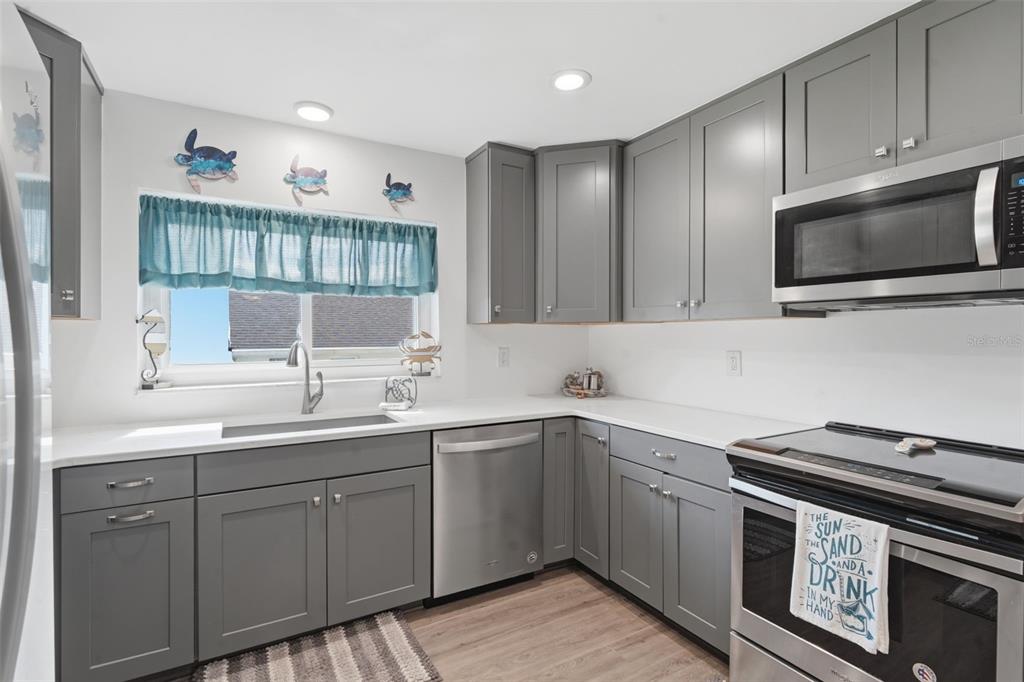A kitchen features gray shaker cabinets, white countertops, stainless steel appliances, and a window above the sink — 82 JENNIFER CIRCLE, PONCE INLET, FL