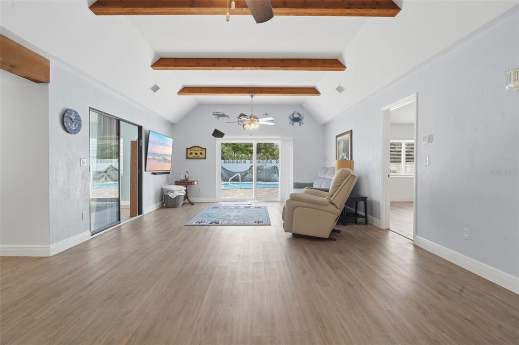 A living room features vaulted ceilings with exposed wooden beams, light flooring, and sliding glass doors — 82 JENNIFER CIRCLE, PONCE INLET, FL