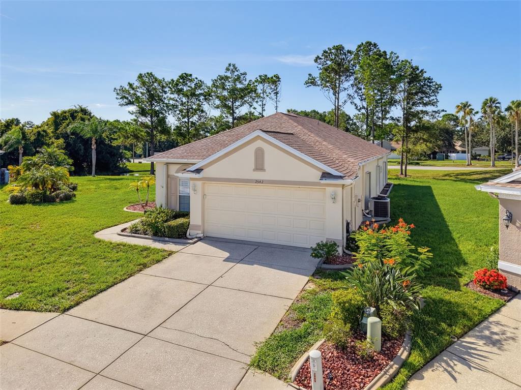 An exterior view of a single-story house with a beige facade and a concrete driveway — 2542 SANDY HILL COURT, HOLIDAY, FL