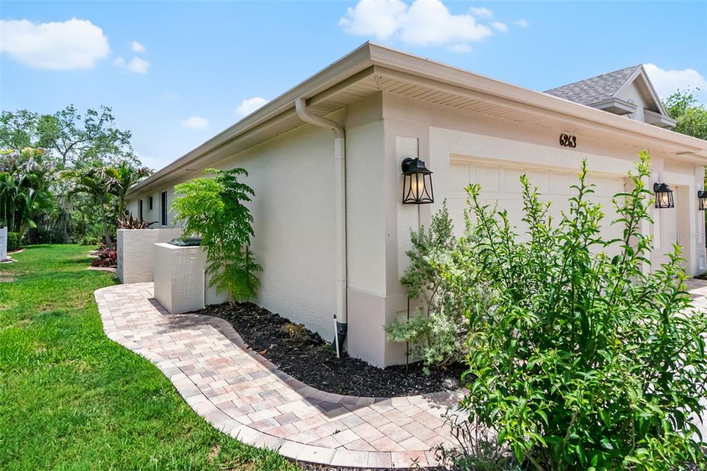 A side view of a beige house exterior with a paver walkway and landscaping — 6263 AVENTURA DRIVE, SARASOTA, FL
