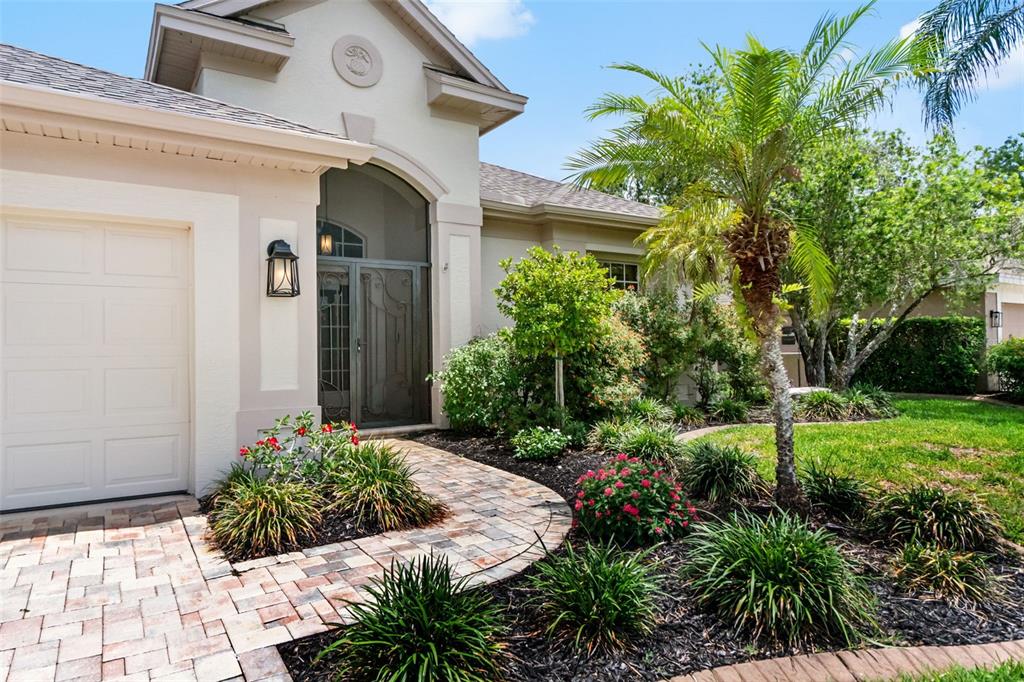 A beige house exterior features a brick paver walkway, a palm tree, and landscaping — 6263 AVENTURA DRIVE, SARASOTA, FL