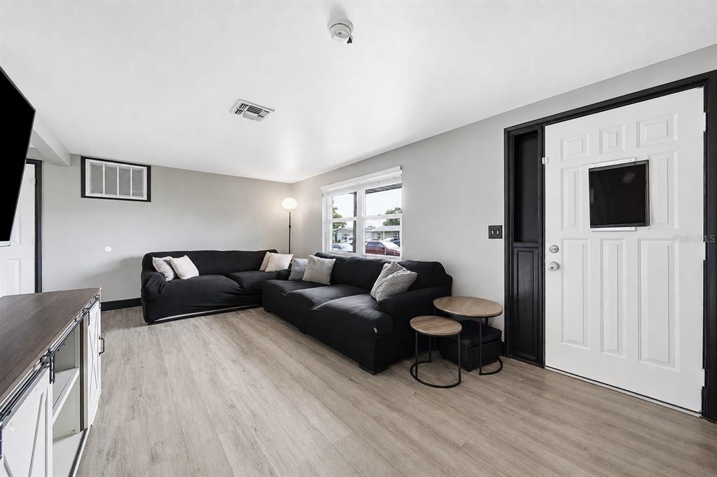 A living room features light wood-look flooring, a black sectional sofa, and a white door — 3622 WINDER DRIVE, HOLIDAY, FL