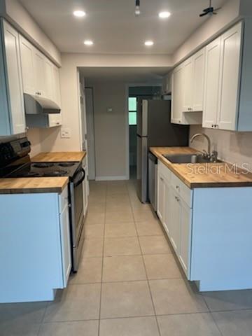 A galley kitchen features white cabinets, butcher block countertops, and stainless steel appliances — 208 MAGNOLIA AVENUE UNIT B, ANNA MARIA, FL