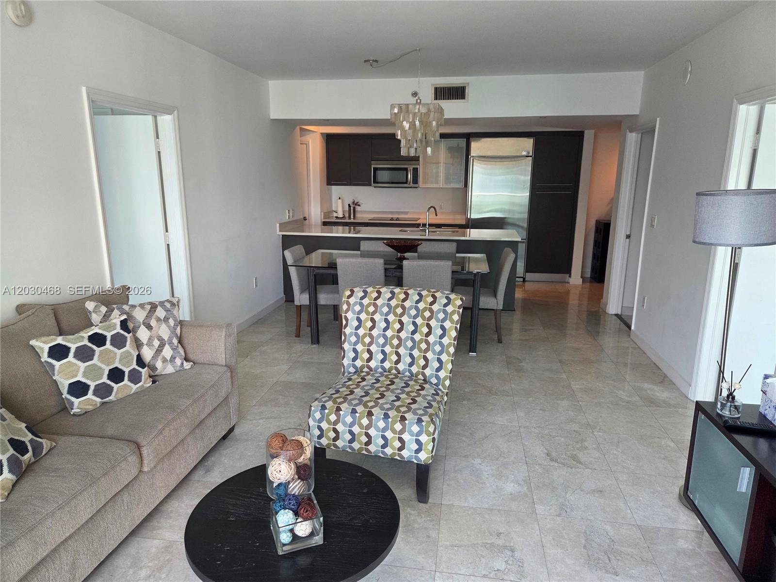 A living room with a sofa and patterned chair opens to a kitchen with dining area — 500 Brickell Ave # 3105, Miami FL 33131, MIAMI, FL