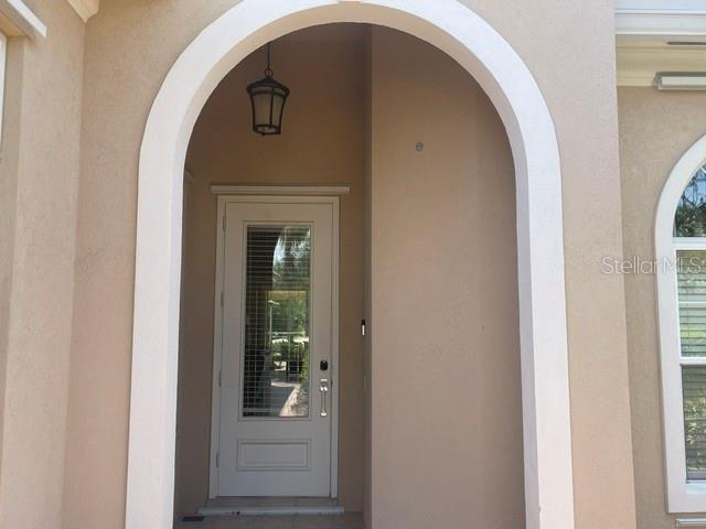 An arched entryway features a beige stucco wall, a hanging lantern, and a glass-paneled door — 11818 FIORE LANE, SARASOTA, FL