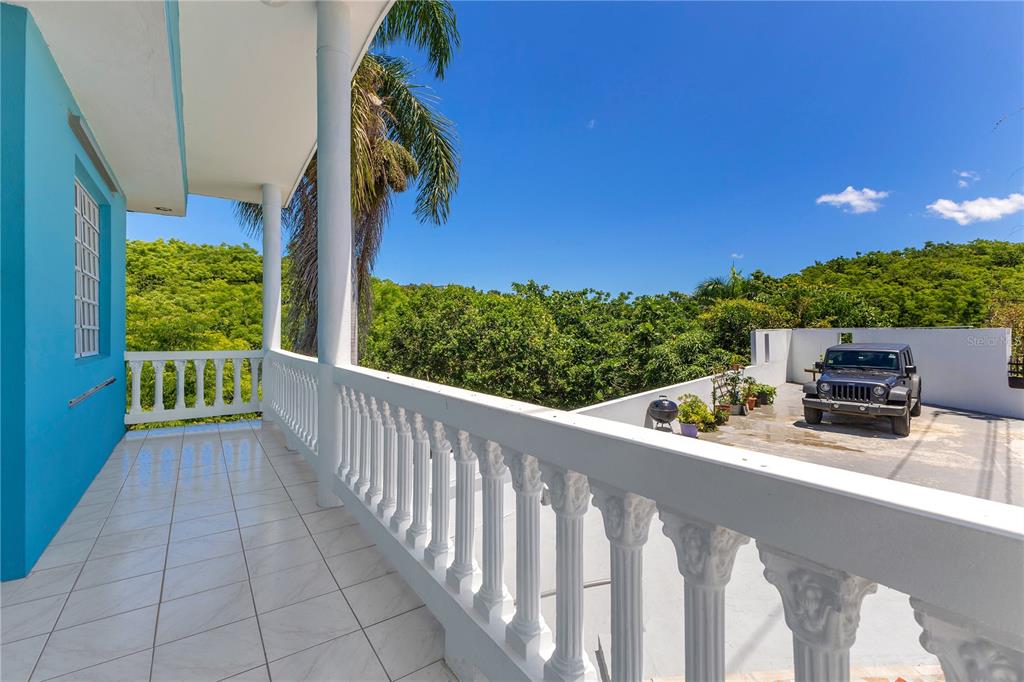 A tiled balcony with white balustrades overlooks a driveway with a parked Jeep and trees — 1 CAMINO MORTERO, RINCON, PR