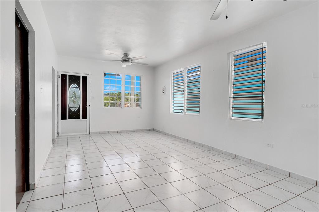 An empty room features white walls, white tiled floors, a ceiling fan, and louvered windows — 1 CAMINO MORTERO, RINCON, PR