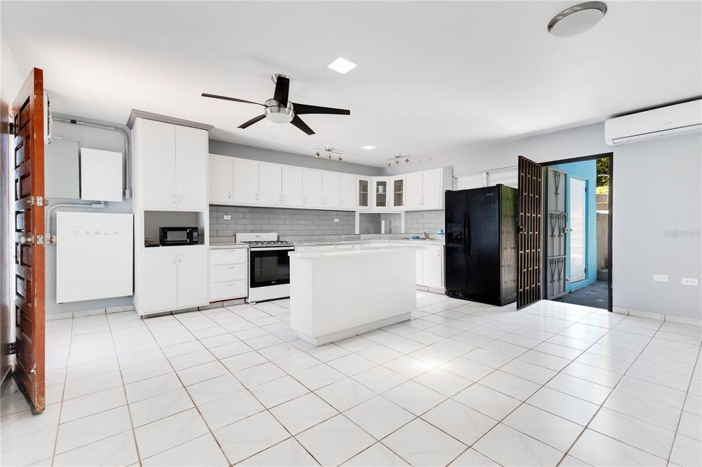 A kitchen with white cabinets, a central island, black appliances, and a Tesla Powerwall unit — 1 CAMINO MORTERO, RINCON, PR