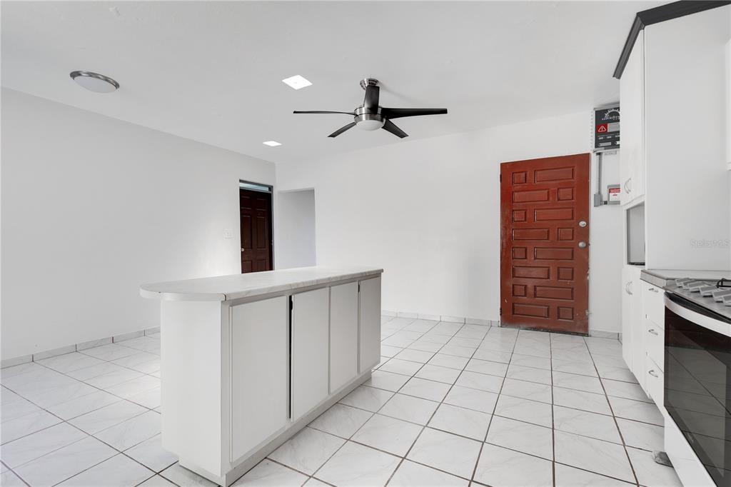 A kitchen features white cabinets, a central island, white tile flooring, and a red door — 1 CAMINO MORTERO, RINCON, PR