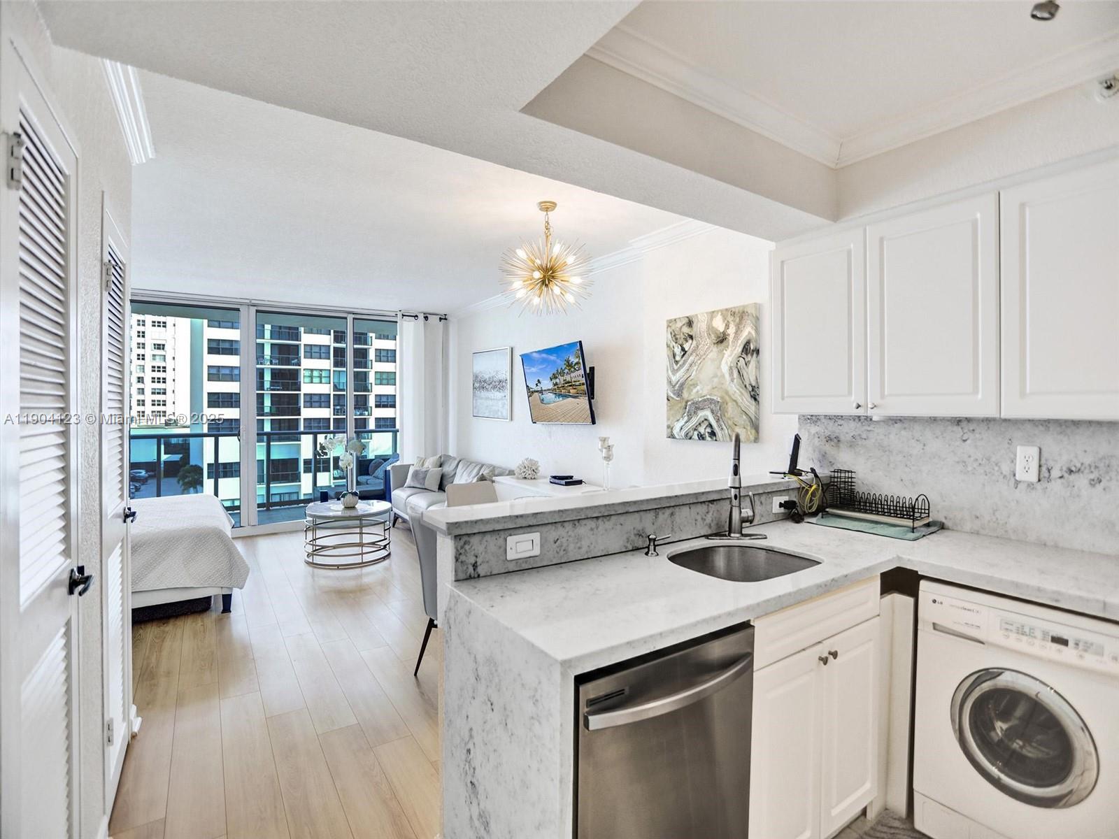 A kitchen with white cabinets and marble countertops overlooks a living area with a balcony — 2501 S Ocean Dr # 505, Hollywood FL 33019, HOLLYWOOD, FL